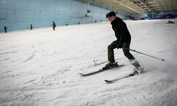A man in black ski clothing, skiing down the snowy slope at chill factore indoor ski slope