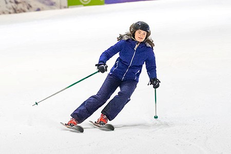 A young person skiing down a ski slope and smiling, they are wearing a blue ski jacket and trousers