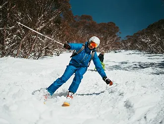 Front view of person skiing downhill on an outdoor ski slope wearing blue skiing attire and a ski helmet.