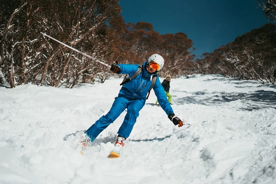 Front view of person skiing downhill on an outdoor ski slope wearing blue skiing attire and a ski helmet.