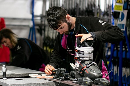 Man in black jumper looking at ski boot attached to skiis with other staff in the background