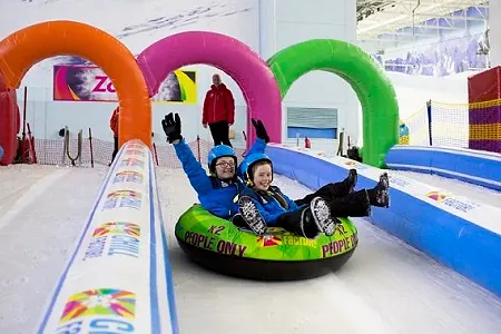 Two children sliding down a snow slope in a downhill donut ring