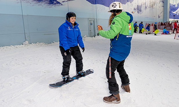 A snowboarder stood in the snow, facing their chill factore snowboarding instructor