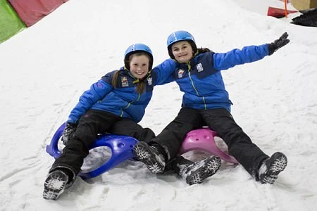 2 children enjoying sledging on an indoor slope slope