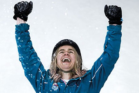 Person wearing ski gear and a helmet holding their arms aloft in celebration