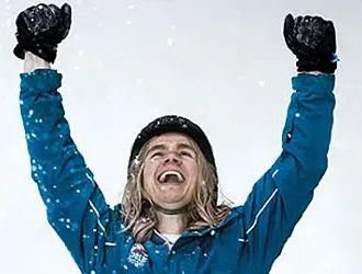 Woman in snow wearing skiing gear, smiling with raised arms raised as if enjoying the mental benefits of skiing