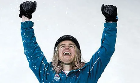 Woman in snow wearing skiing gear, smiling with raised arms raised as if enjoying the mental benefits of skiing